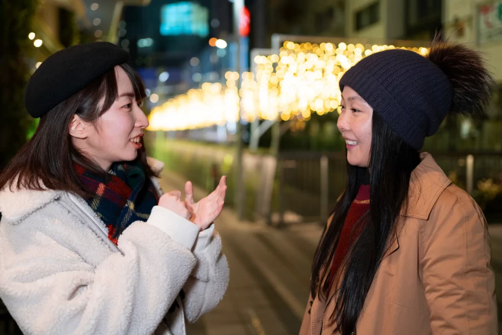 Two women having a conversation in Japanese on a brightly lit street at night, practicing essential Japanese travel phrases for smooth communication in Japan.