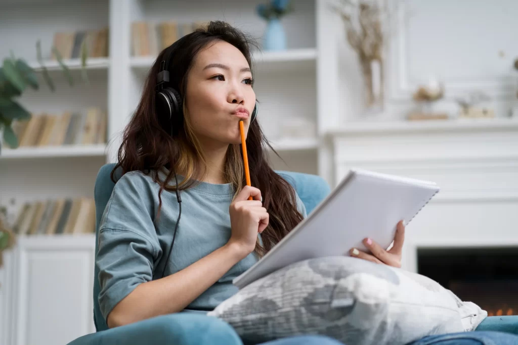 Young woman practicing to improve her Japanese speaking skills by listening to audio exercises and taking notes at home.