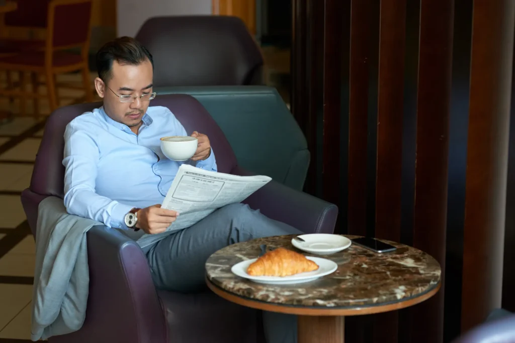 asian-man-reading-morning-tabloid-legs-crossed-coffeshop